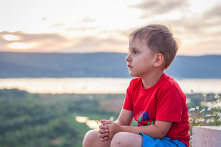 Cute Boy in a red T-shirt on the background of a stunning sunset. Journey. The face expresses natural joyful emotions. Not staged photos from nature.の写真素材