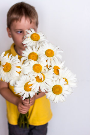 A cute boy with a beautiful bouquet of large daisies. Portrait of a child, funny and cute facial expression. selective focus. A postcard for the celebration of the day of family, love and fidelity.の写真素材