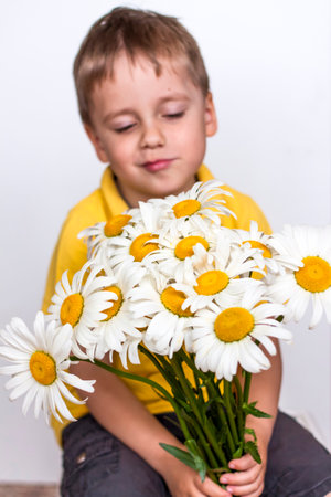 A cute boy with a beautiful bouquet of large daisies. Portrait of a child, funny and cute facial expression. selective focus. A postcard for the celebration of the day of family, love and fidelity.の写真素材