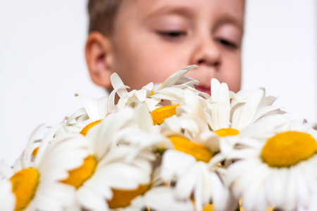 A cute boy with a beautiful bouquet of large daisies. Portrait of a child, funny and cute facial expression. selective focus. A postcard for the celebration of the day of family, love and fidelity.の写真素材