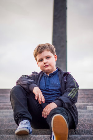 The boy is sitting on the steps in the open air against the background of skyscrapers and high-rise buildings. Journey. Lifestyle in the city. Center, streets.の写真素材