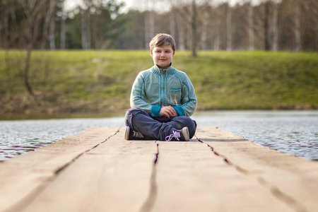 A boy is sitting on a bridge in a green park. The path is a bridge over the lake. long wooden flooringの写真素材