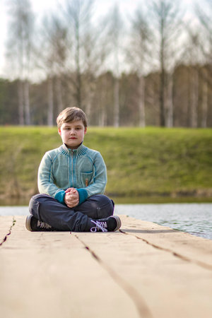 A boy is sitting on a bridge in a green park. The path is a bridge over the lake. long wooden flooringの写真素材