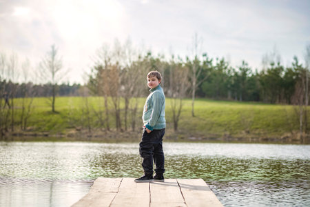 A boy walks along a path in a green park. The path is a bridge over the lake. long wooden flooringの写真素材