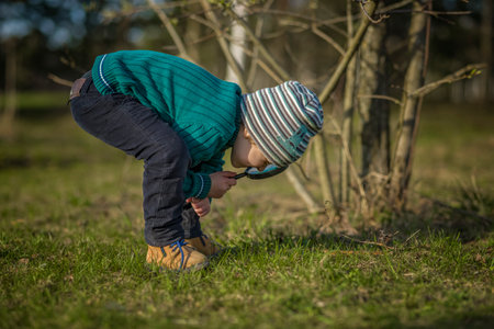 A funny boy walks through the spring park, examines the leaves with a large magnifying glass, looks for bugs and enjoys. A happy child. Portraitの写真素材