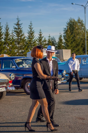 2022-08-12 Tatarstan, Verkhneuslonsky district, Savino village. Resort town "Sviyazhsky hills". Kazan Festival of Historical Cars. A man and a woman in retro clothes pose near carsのeditorial素材