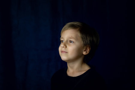 A concise portrait of a European boy. Portrait on a dark background. A strict frame.の写真素材