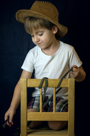 A concise portrait of a European boy. Portrait on a dark background of a boy in a cowboy hat and a white T-shirt. A strict frame.の写真素材