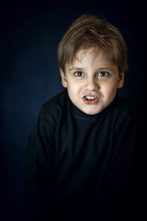 A concise portrait of a European boy. Portrait on a dark background. A strict frame.の写真素材