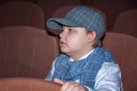 A cute teenage boy in a cap and a plaid scarf. The image of a detective. Magnifying glass in hand. Playing on stageの写真素材