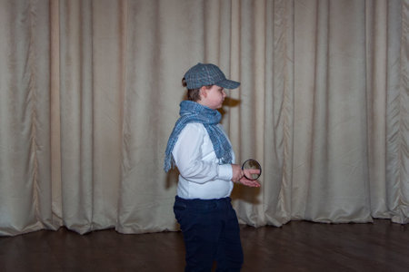 A cute teenage boy in a cap and a plaid scarf. The image of a detective. Magnifying glass in hand. Playing on stageの写真素材