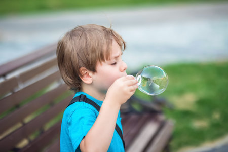 A happy boy blows soap bubbles in the park on a sunny summer day.