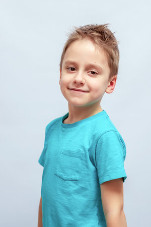 Smiling young boy with short brown hair wearing a blue t-shirt, standing with a slightly tilted head. The boy's expression is relaxed and cheerful, conveying warmth and approachabilityの写真素材