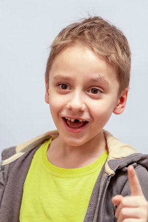 Young boy with short light brown hair smiling and pointing, wearing a lime green shirt under a gray hoodie. He has a missing tooth and a joyful expression, looking slightly to the sideの写真素材