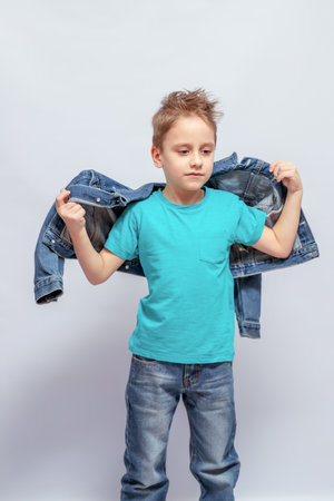 Young boy with short hair putting on or taking off a denim jacket, wearing a turquoise T-shirt and blue jeans. He stands confidently with a neutral expression, indoorsの写真素材