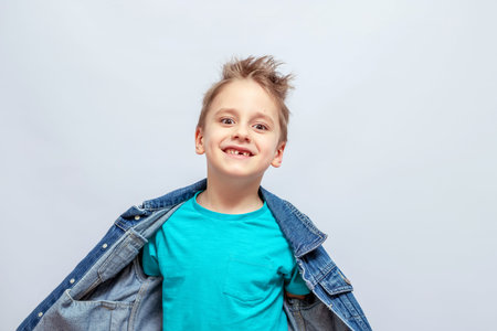 Smiling young boy with spiky hair, wearing a bright blue t-shirt and an open denim jacket. He stands confidently with a playful expression and direct eye contactの写真素材