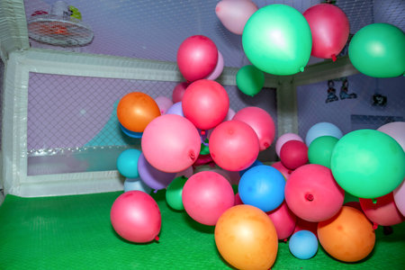 Colorful balloons of various sizes are scattered across a green play area, enclosed by a netted fence. Bright hues of pink, blue, green, and orange are prominently featuredの写真素材