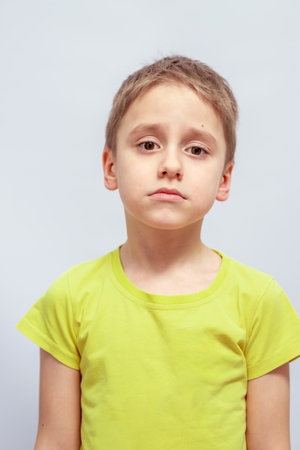 Young child with short hair wearing a light green t-shirt looks slightly sad. The child stands facing the camera with visible facial features conveying a thoughtful expressionの写真素材