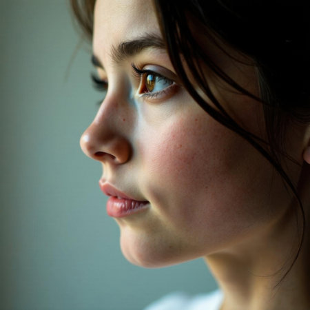 Close-up of a young woman's profile with focus on her expressive brown eyes, light freckles, and soft features. Her dark hair partially frames her face, creating a gentle, contemplative lookの素材