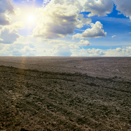 plowed field and sun on cloudy skyの写真素材
