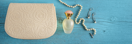 A handbag and a bottle of perfume on a blue wooden background. View from above. Flat lay. Wide photo.の写真素材