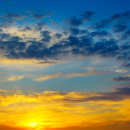 A bright sunrise in the sky with cumulus clouds.の写真素材