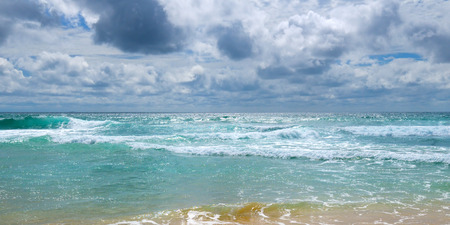 The sandy beach of the tropical ocean and the overcast sky with dramatic clouds. Wide photo.の写真素材