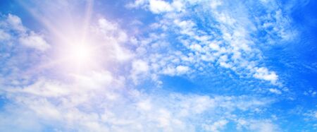 Couds in the blue sky. Bright midday sun illuminates the space. Wide photo.の写真素材