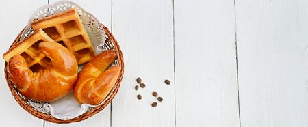 Croissants and waffles in a wicker basket on a white wooden table.の写真素材