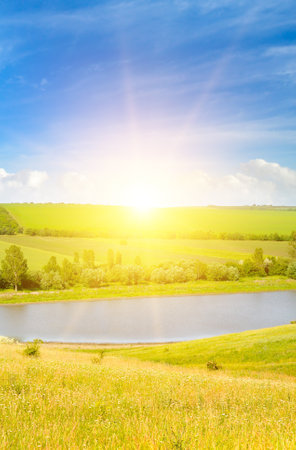 Lake, agricultural field and bright sunrise. Vertical photo.の写真素材