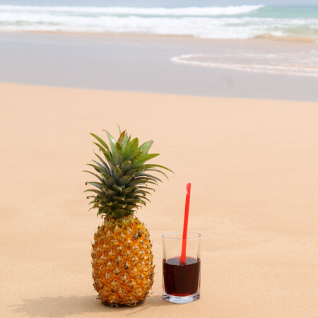 Ripe pineapple and juice in a glass on a sandy beach. Concept - vacation and travel.の写真素材