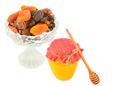 A selection of dried fruits in a vintage crystal fruit bowl and bee honey isolated on white background. Collage. There is free space for text.の写真素材