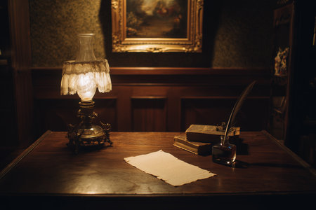 A glowing, lace-shaded antique oil lamp casts warm light on a wooden desk, where a quill pen and inkwell sit beside stacked books and an old manuscript. The low-key lighting and classic period setting evoke a mood of mystery, writing, and history.の素材