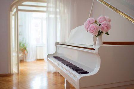 A beautiful white grand piano with a small vase of lush pink peonies sits in a sunny room with high ceilings and sheer white curtains, with the focus on elegance and classical music. The bright, soft lighting and minimalist interior convey a sense of calmness and sophistication.の素材