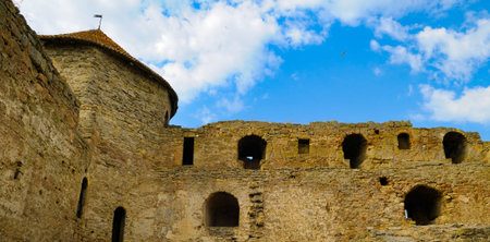 A low-angle view captures the rough, weathered stone walls of an ancient medieval fortress and a...