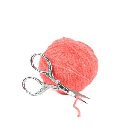 A soft pink ball of wool yarn paired with ornate vintage silver scissors isolated on white. This...