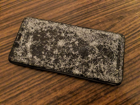Mobile phone with broken glass on a dark wooden background