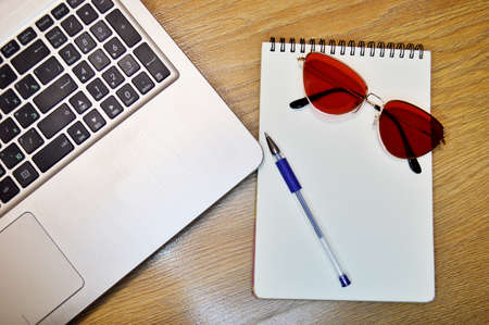 Mix of office supplies and gadgets on a wooden table background. View from above. laptop, pen, notebook and glasses on a wooden backgroundの写真素材
