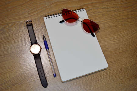 Mix of office supplies and gadgets on a wooden table background. View from above. Wrist Watch, notebook, pen and glasses on wooden backgroundの写真素材
