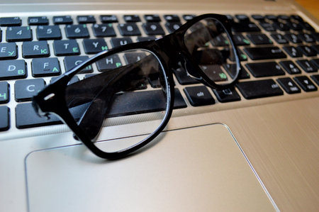 Glasses lie on a black laptop keyboard close-up. A break during work