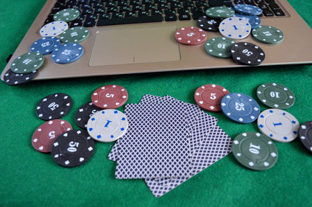 Poker chips and cards lie on a laptop keyboard with a green screen on a green background