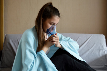 Young beautiful girl with dark hair sits wrapped in a plaid with a blue plastic maskの写真素材