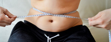 Close-up of female belly with measuring tape around it