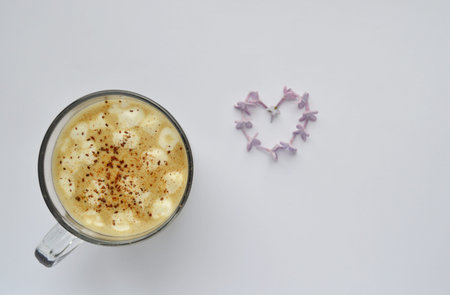 cappuccino with marshmallows and cinnamon on a white background. Heart shape purple lilac flowers on...
