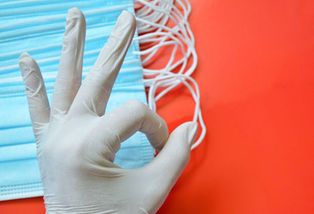 Hand in white glove shows okay symbol on a background of blue medical masks.