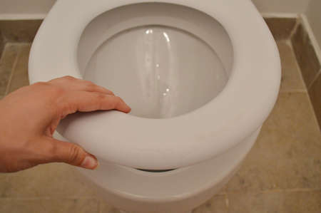 Modern White toilet bowl in a bathroom. Female hand picks up the white rim of the toilet bowlの写真素材