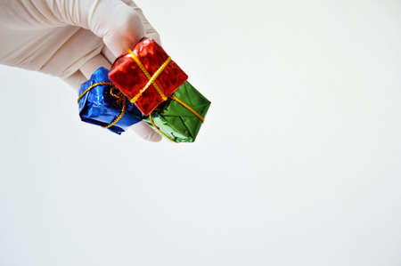 Female hand in white rubber gloves holds red, blue and green gifts on a white backgroundの写真素材