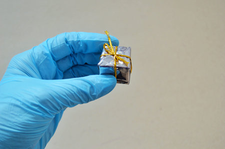 Female hand in blue rubber gloves holding a gray gift on a gray background.