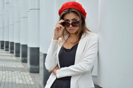 Beautiful business woman on the background of the modern office. Portrait of a girl with dark hair in a white jacket and a red beret near the business centerの写真素材