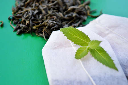Tea bags, loose tea and fresh mint leaves on a green backgroundの写真素材